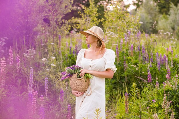 Foto giovane donna con cappello di paglia e vestito con un bouquet di fiori di lupino