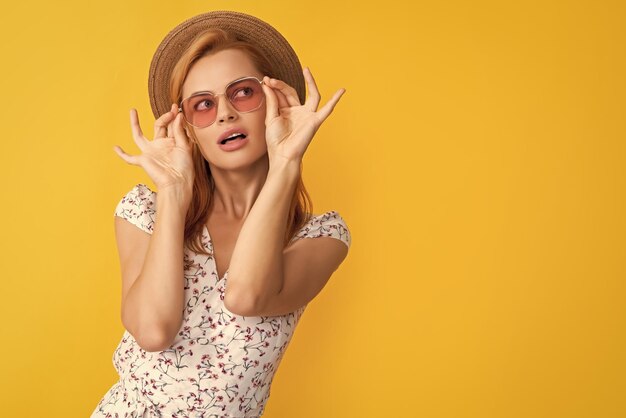 Young woman in straw hat and sunglasses on yellow background