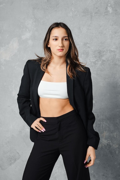 Young woman in street style outfit posing in studio on grey canvas background