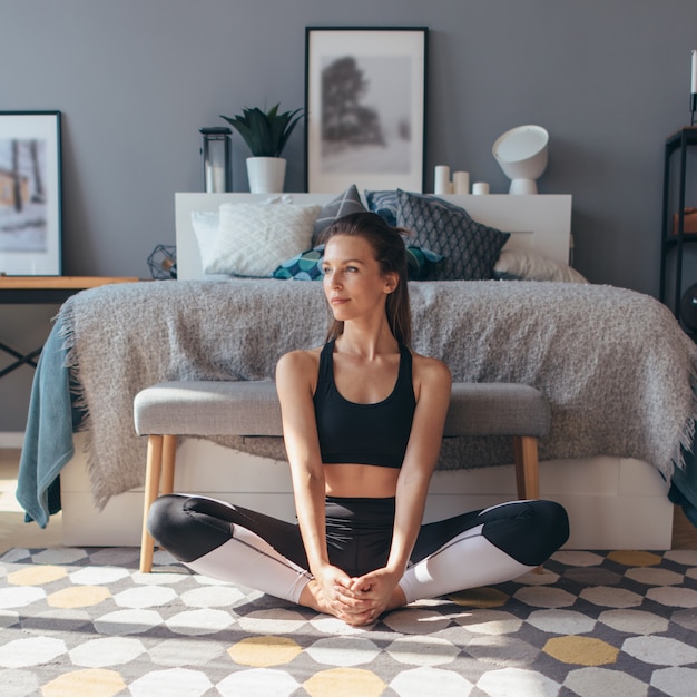 Young woman stretches her legs with her knees apart.