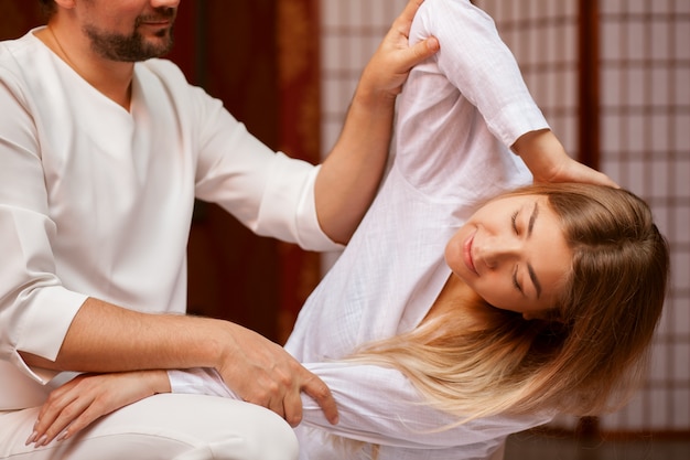 Young woman stretching her body with the help of professional thai massage therapist at spa center. Male masseur performing thai massage on his client. Recreation, relaxation, healing 