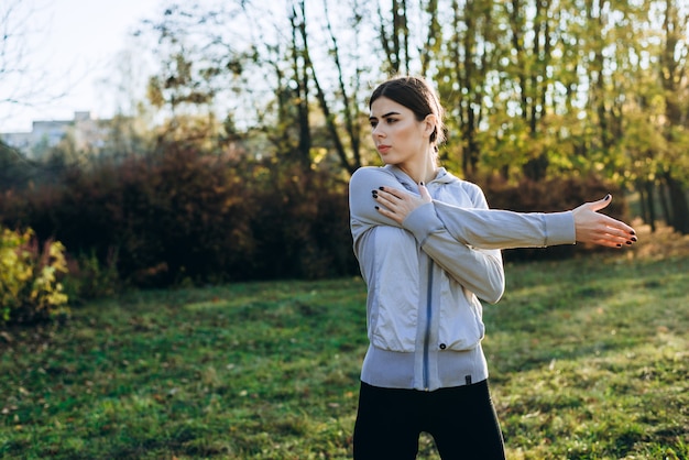 Giovane donna che allunga e che si scalda nel parco. ragazza attraente che allunga prima della forma fisica.