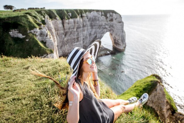 Young woman in striped hat enjoying great view on the famous rocky coastline near Etretat town in France