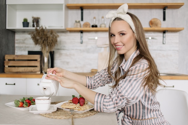 A young woman in striped pajamas is having Breakfast in the kitchen