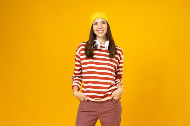 A young woman in a striped tshirt with headphones is smiling on a yellow background