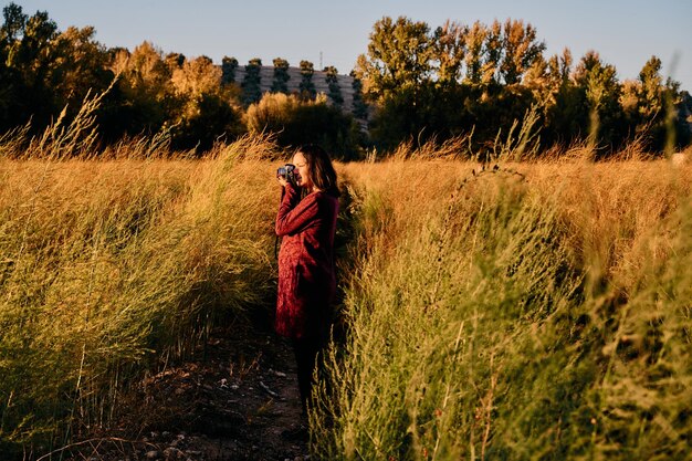 夕暮れ時にビンテージカメラを持って田園地帯を散歩する若い女性