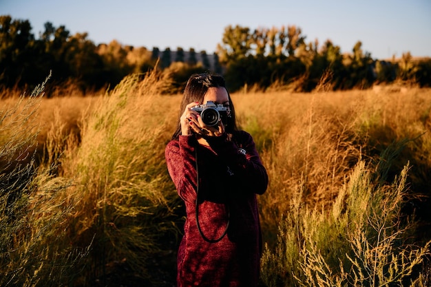 Photo a young woman strolling through the countryside with her vintage camera at sunset