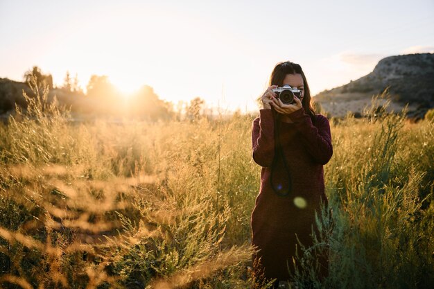 Photo a young woman strolling through the countryside with her vintage camera at sunset