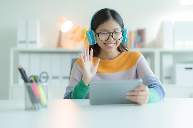 Молодая женщина или студентка, использующая планшетный компьютер в библиотеке в очках и наушниках. Она улыбается и выглядит счастливой.