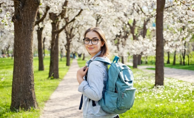 Фото Молодая студентка с рюкзаком гуляет в парке весной студент фрилансер в куртке джинсы гуляет в весеннем парке на открытом воздухе отдыхает