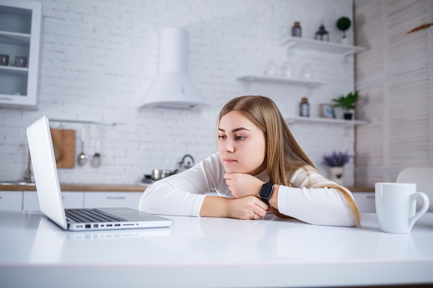 Young woman studies at home in the kitchen on a laptop. Work remotely from home