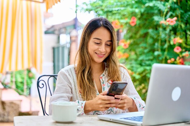 young woman studying with laptop looks at her phone to check social networks