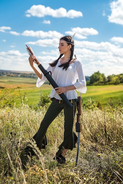 自然の中で弓と矢を保持しているスタイルのネイティブアメリカンインディアンの若い女性