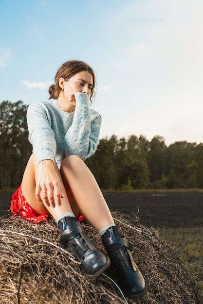 Young woman in stylish clothes sitting on hay