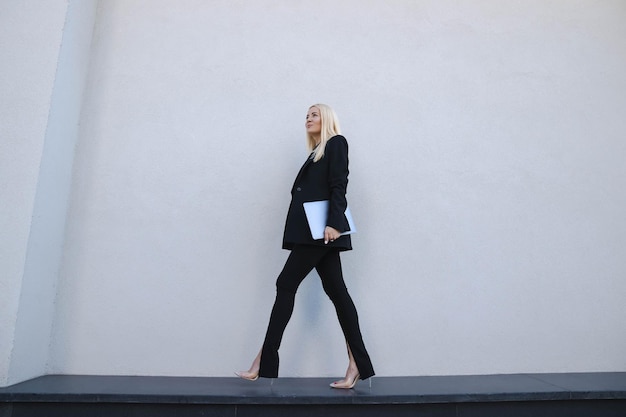 A young woman in a stylish suit with a laptop poses against the background of a business center