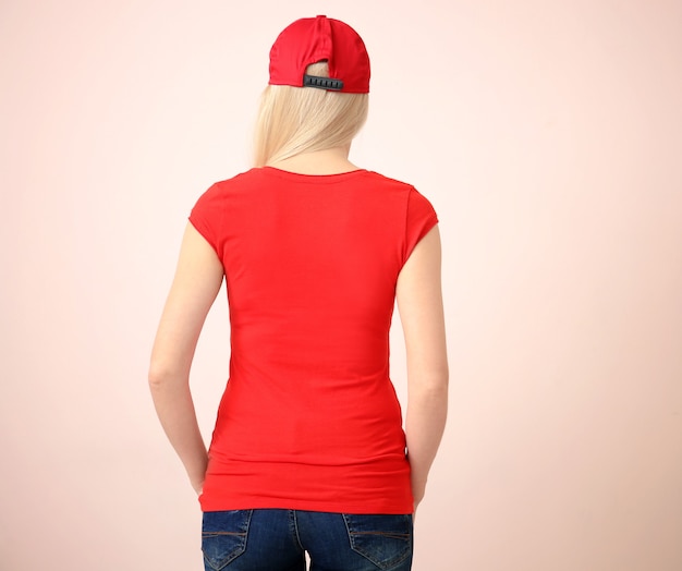 Молодая женщина в стильной футболке и кепке на стене цвета. Мокап для дизайна