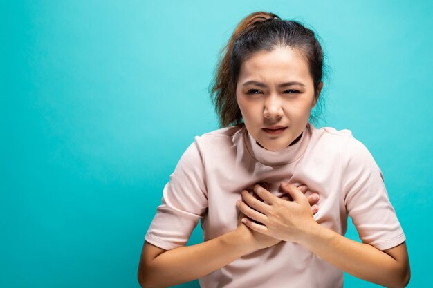 Young woman suffering from chest pain against turquoise background