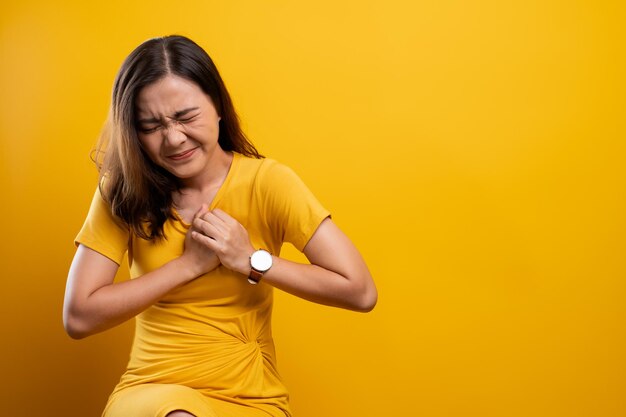 Photo young woman suffering from chest pain sitting against yellow background