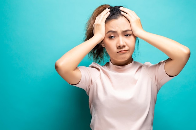 ターコイズ色の背景に頭痛を患っている若い女性