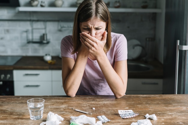 Giovane donna che soffre di nausea con medicine e bicchiere d'acqua sulla scrivania