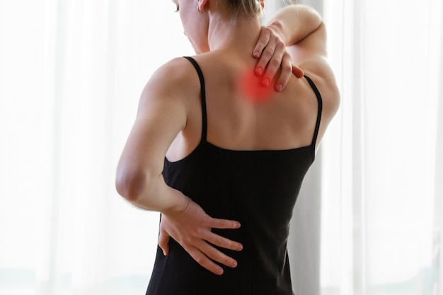首の痛みと背中の痛みに苦しんでいる若い女性、自宅で筋肉を伸ばします。背中と首の痛みの女性