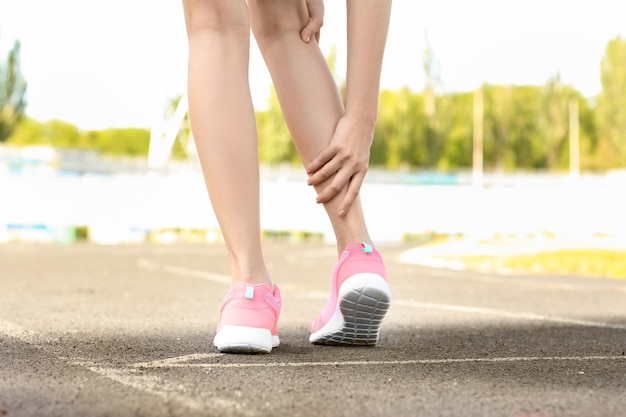 Young woman suffering from pain in leg outdoors