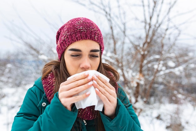 Photo young woman suffering from a seasonal cold and flu blowing her nose on a handkerchief as she stands outdoors on winter healthcare and medical concept