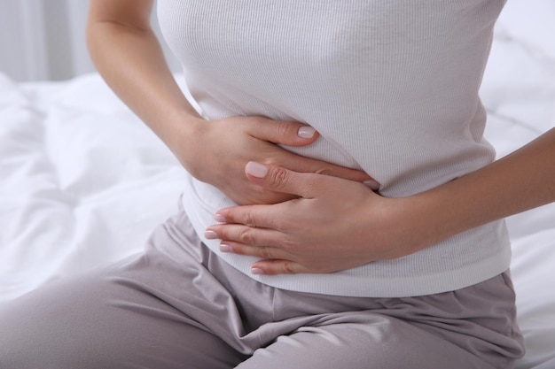 Young woman suffering from stomach ache on bed closeup