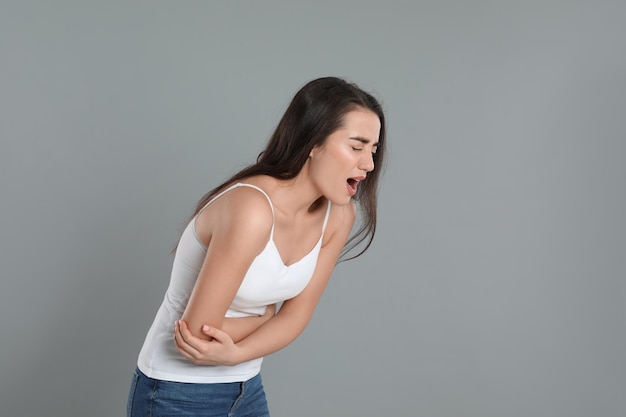 Young woman suffering from stomach ache on grey background Food poisoning