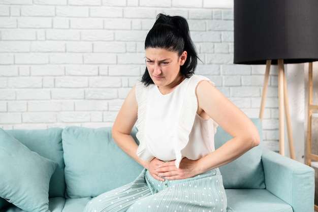 Young woman suffering from stomach ache at home Pain