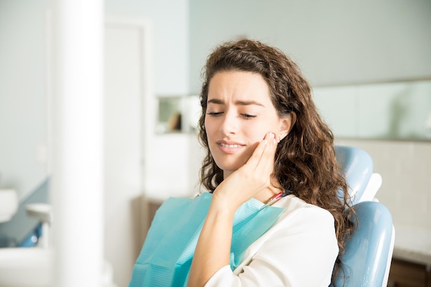 Young woman suffering from toothache while sitting on dental chair in clinic