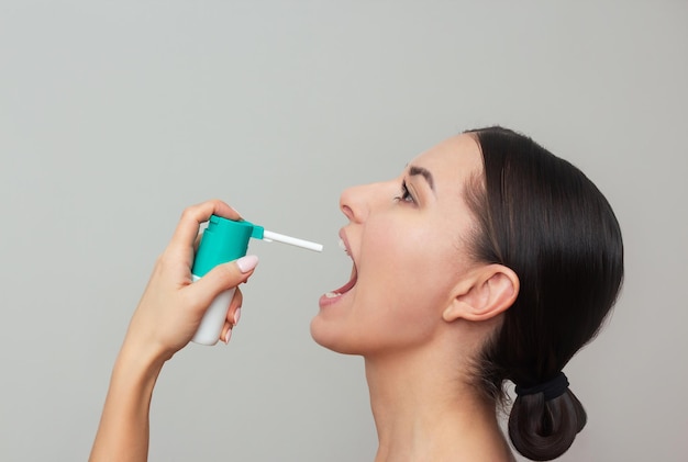 a young woman suffers from a viral or colds disease sprays a sore throat spray into her mouth