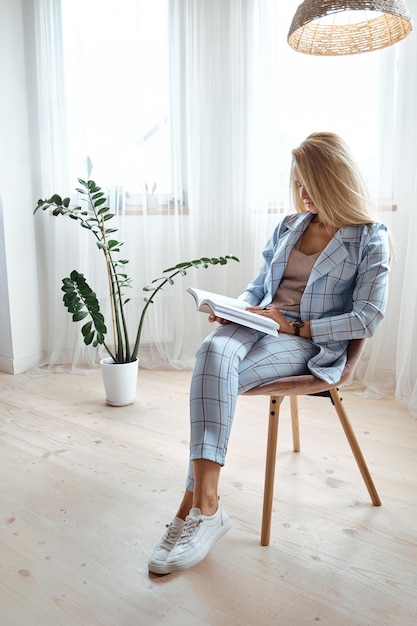 Young woman in a suit reading a book sitting on a chair