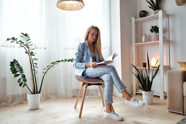 Young woman in a suit reading a book sitting on a chair