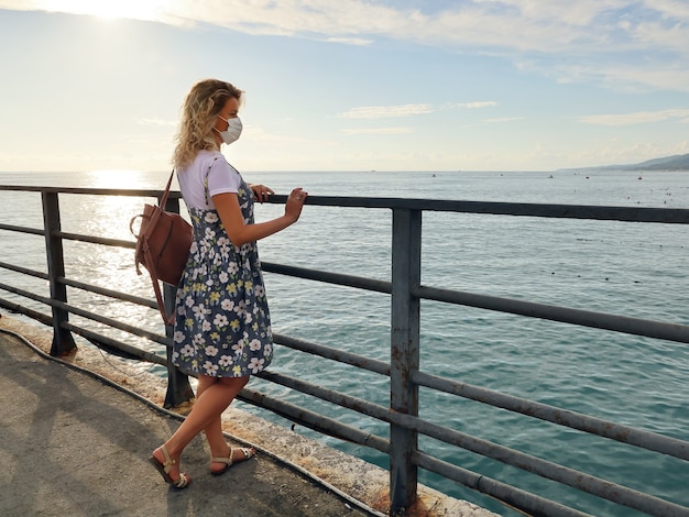 Young woman in summer dress standing on deserted pier and looks at sea