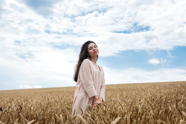 Giovane donna in abito estivo in piedi nel campo di grano e godersi la vita