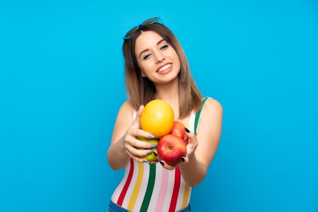 Photo young woman in summer holidays over blue background holding fruits