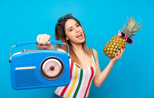 Young woman in summer holidays over blue background holding a pineapple with sunglasses