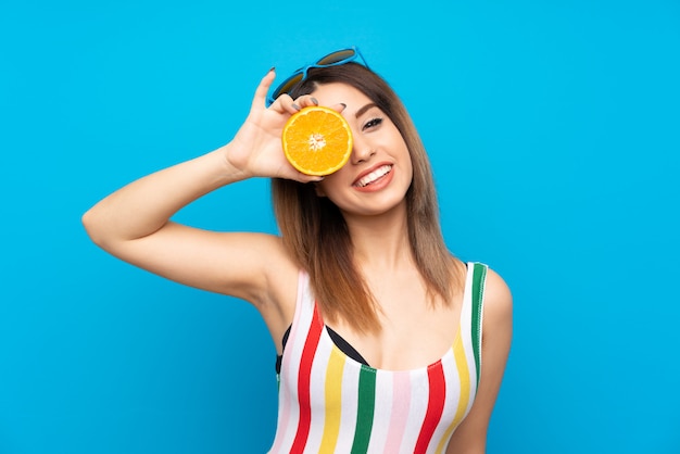 Young woman in summer holidays over blue  holding an orange