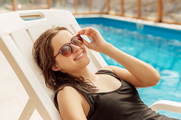 젊은 여자는 수영장 근처 sunbathes