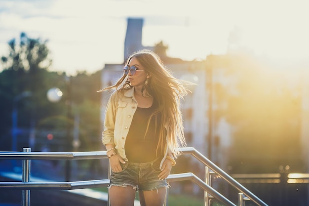 サングラスをかけた若い女性は、バックグラウンドで屋外の夕日を楽しんでいます