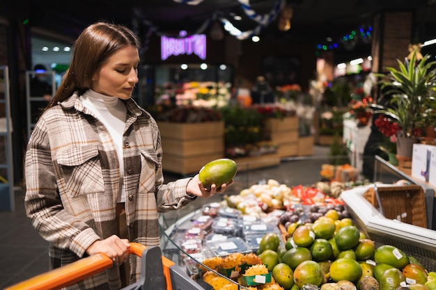 Young woman in supermarket choosing fresh ripe mango