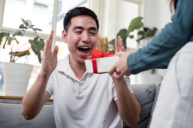 Young woman surprise  boyfriend with a gift box held on the occasion of the anniversary of love.