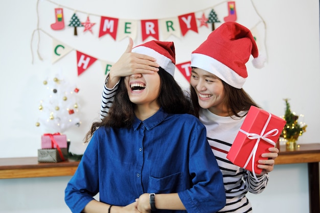 Young woman surprising her girlfriend with christmas gift box. Lesbian couple concept.