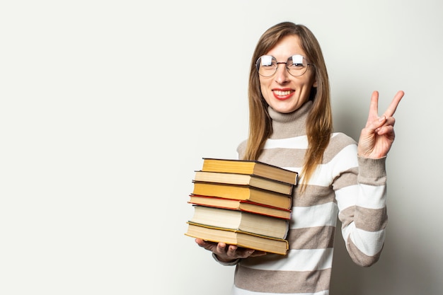 Young woman in a sweater and glasses holding a stack of books