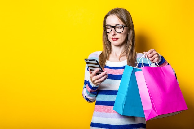 Young woman in sweater holds shopping bags and mobile