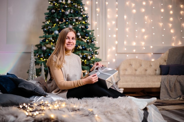 Una giovane donna in un maglione con bei capelli lunghi si siede e ride davanti ai regali di natale felice anno nuovo