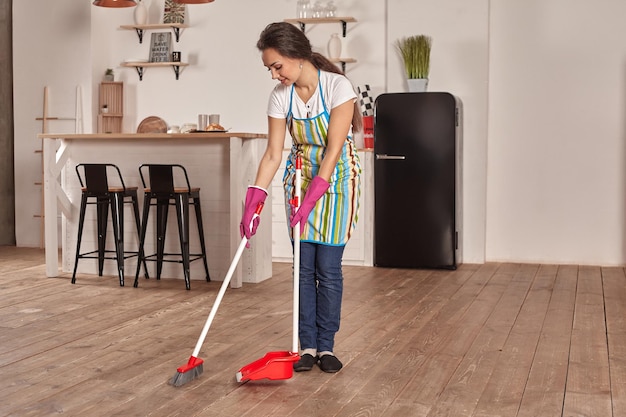 Young woman sweeping floor on the kitchen