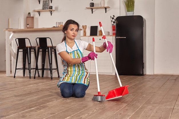 Giovane donna che spazza il pavimento in cucina