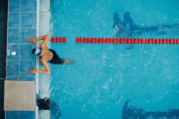 Young woman swimmer swims at swimming pool skirting side